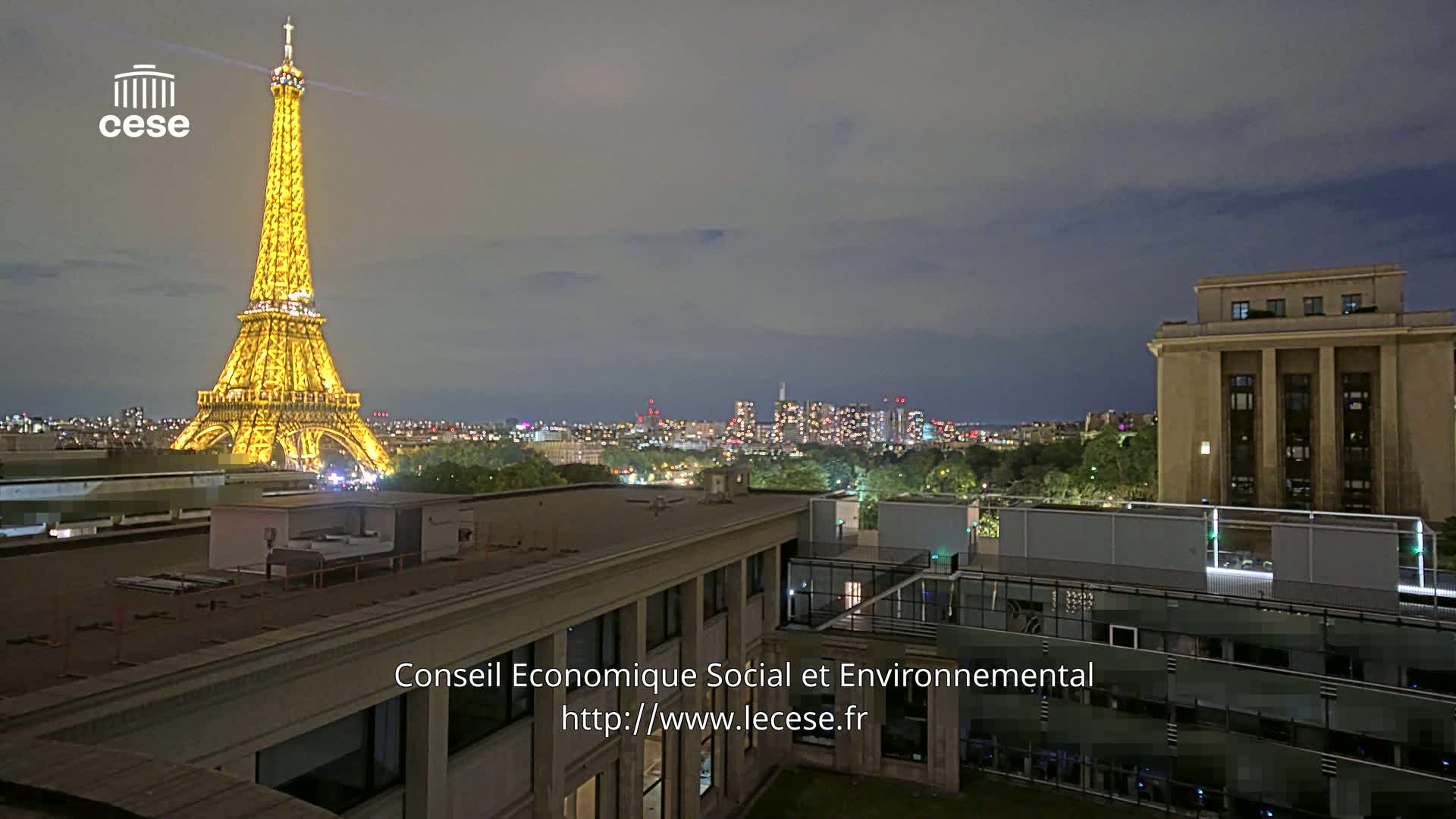 A nighttime view of the Eiffel Tower illuminated against a dusky sky, with a city skyline and rooftops in the foreground.