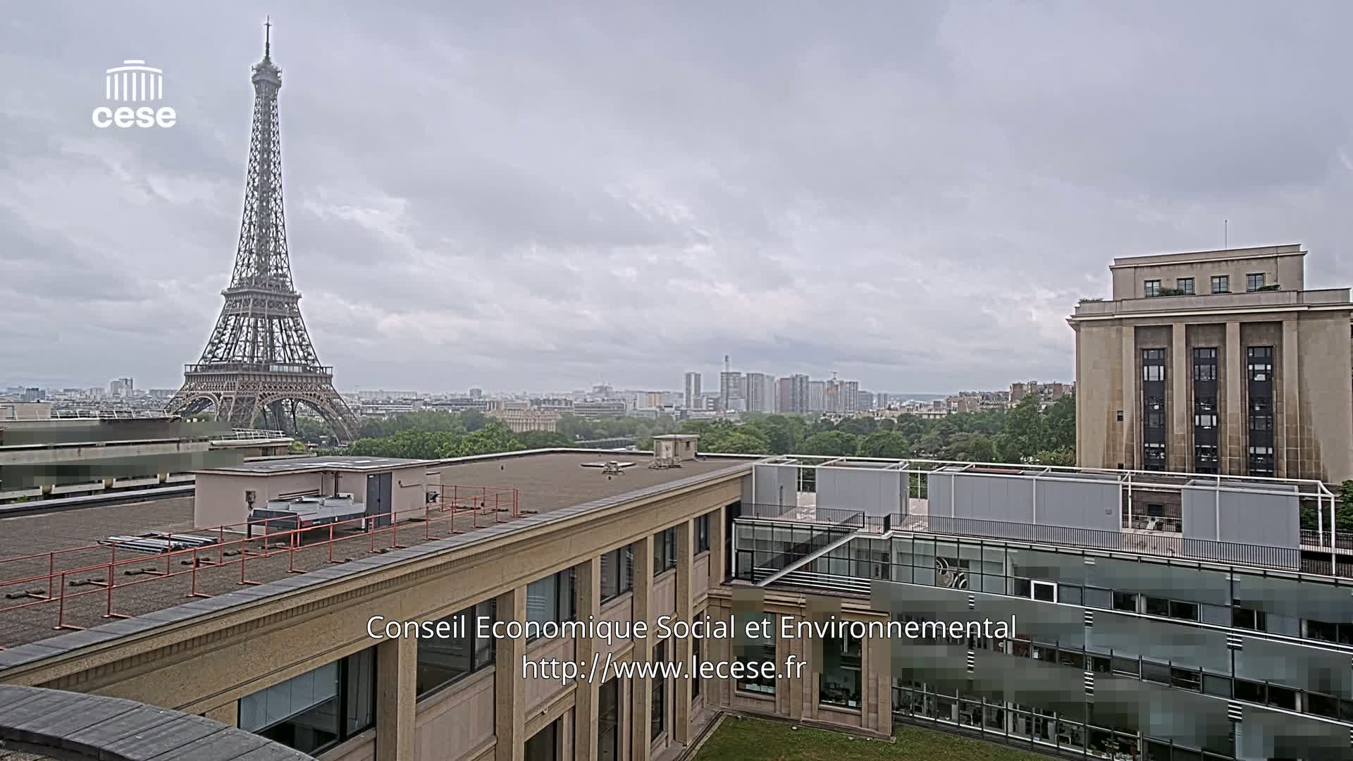 The Eiffel Tower is visible in the distance from a rooftop view of a city under an overcast sky.