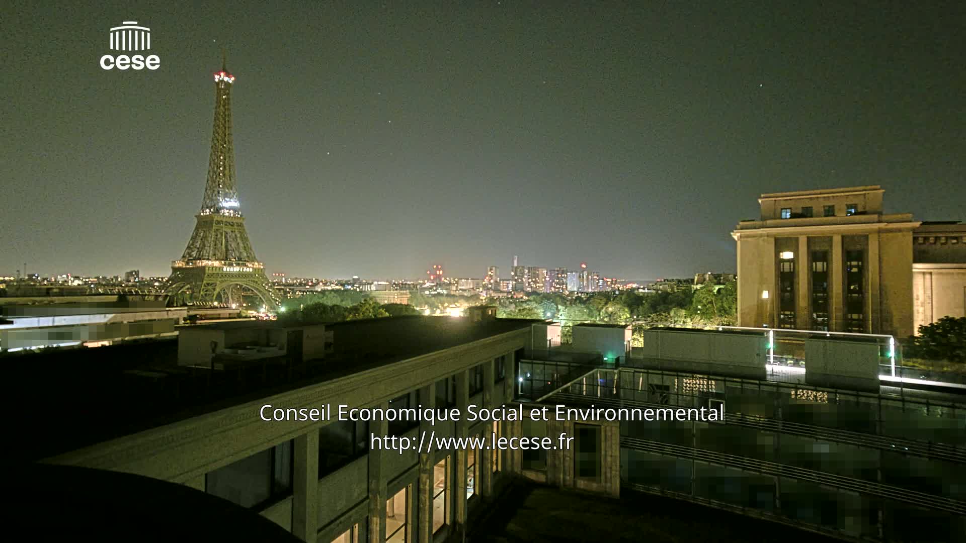 A nighttime view of the Eiffel Tower and a cityscape, with a large building in the foreground under a clear, dark sky.