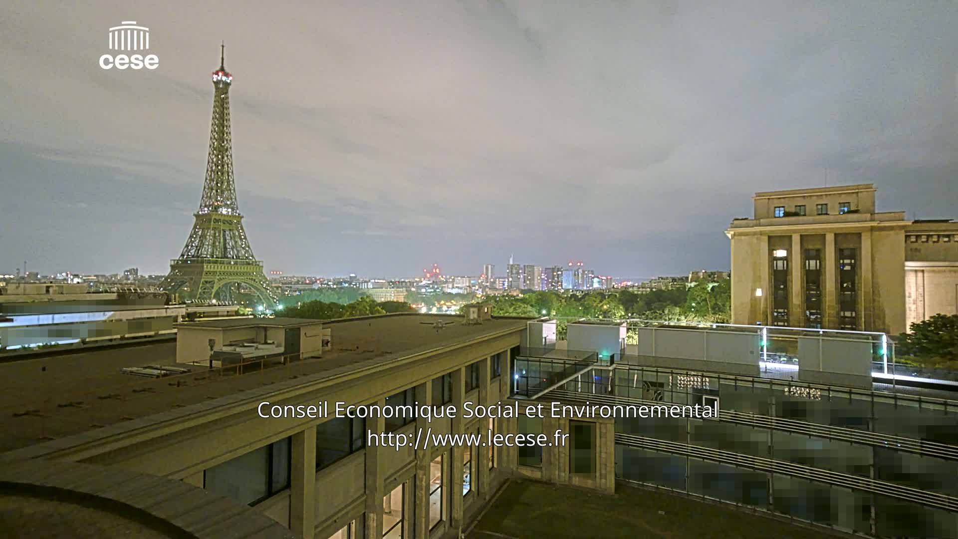 A nighttime view of the Eiffel Tower from a rooftop, showcasing a city skyline under a cloudy sky.
