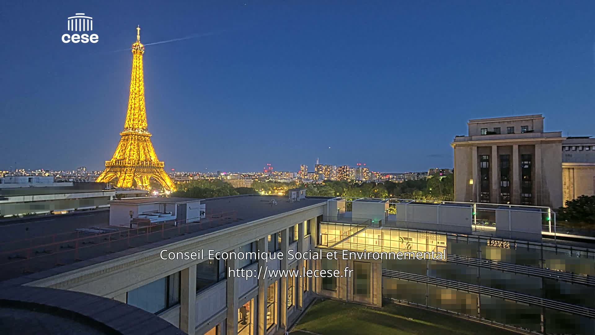 The Eiffel Tower is illuminated at night, with a city skyline visible in the background under a clear, dark blue sky.