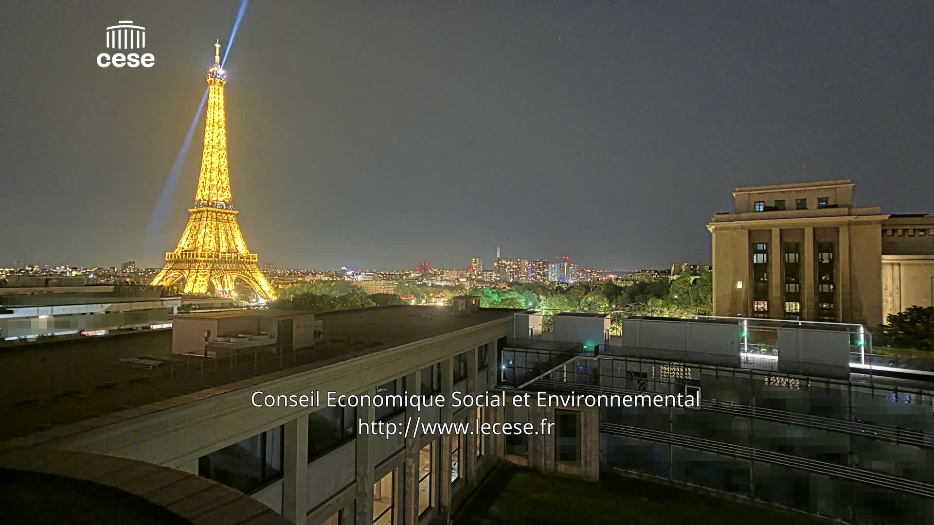 A nighttime cityscape featuring the Eiffel Tower illuminated, a large building to the right, and a city skyline in the distance under a clear sky.