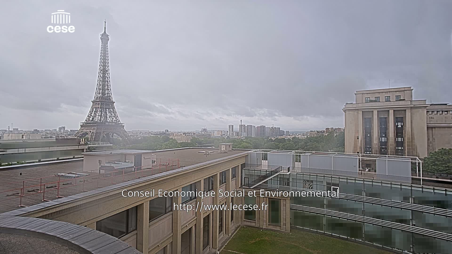A view of the Eiffel Tower in the distance on an overcast day, seen from atop a building with a courtyard and another large building to the right.