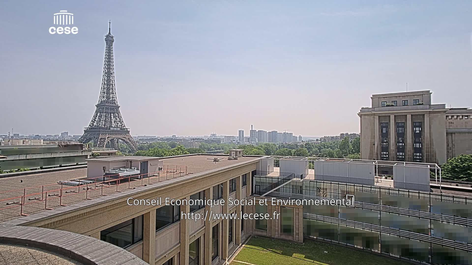 A rooftop view of Paris on a clear, sunny day shows the Eiffel Tower in the distance.