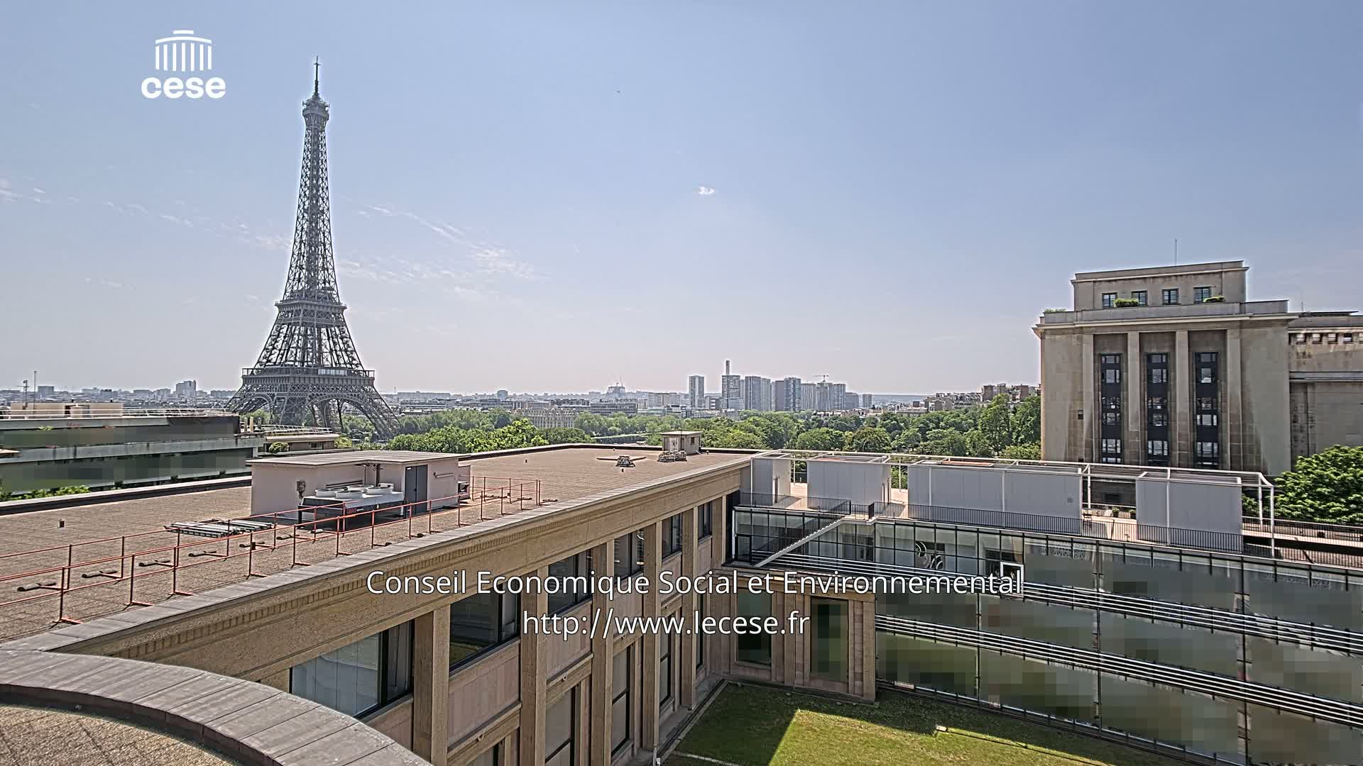 A rooftop view on a clear, sunny day shows the Eiffel Tower in the distance, along with other buildings and greenery.