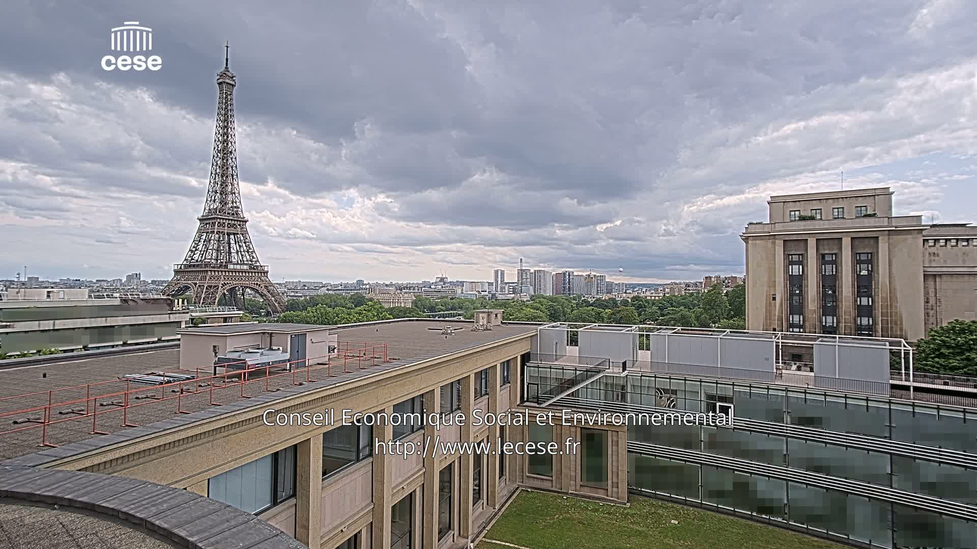 An overcast sky overlooks a cityscape including the Eiffel Tower and modern buildings from a rooftop vantage point.