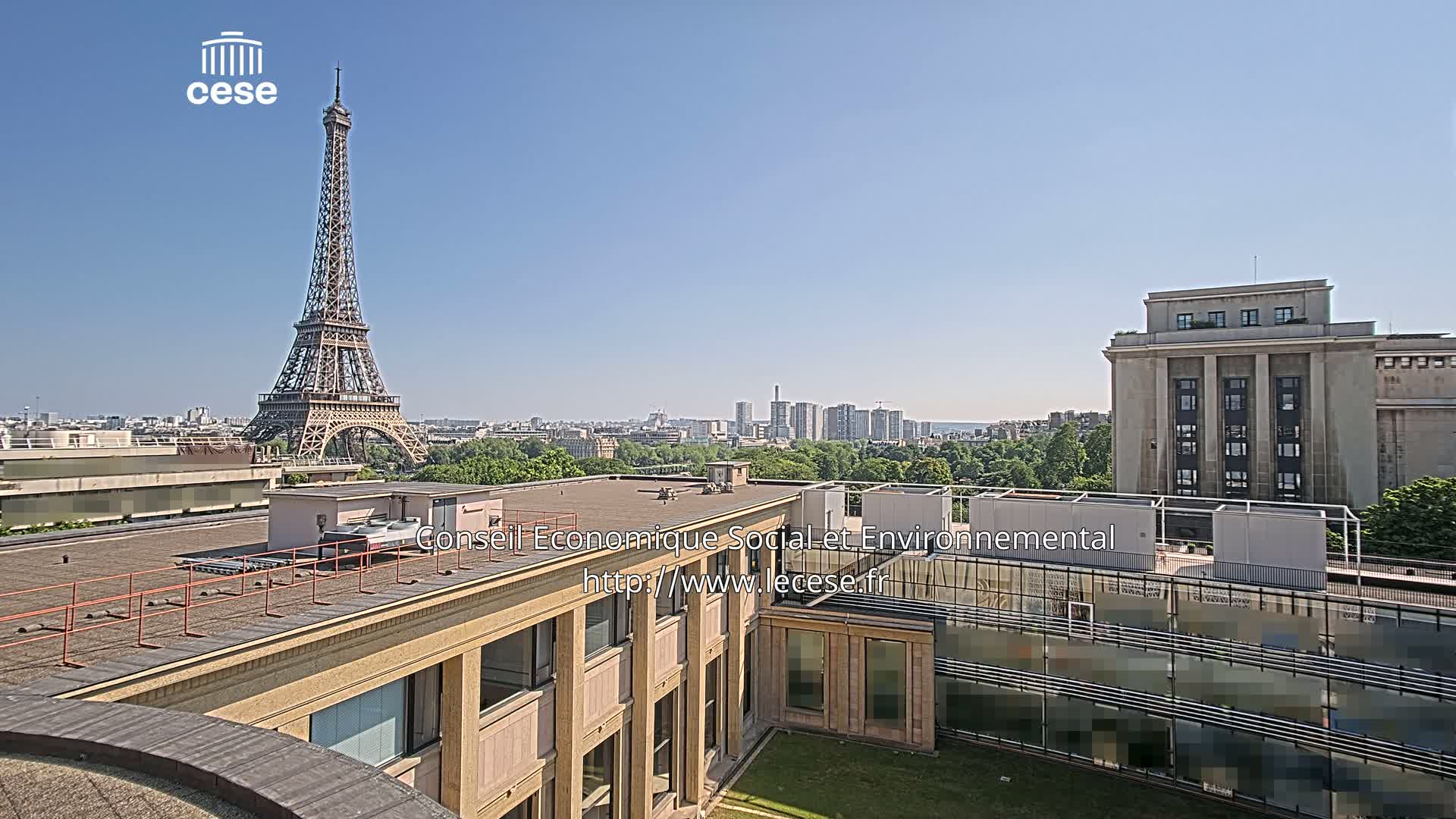 A rooftop view of Parisian buildings on a clear, sunny day, showing the Eiffel Tower in the distance.