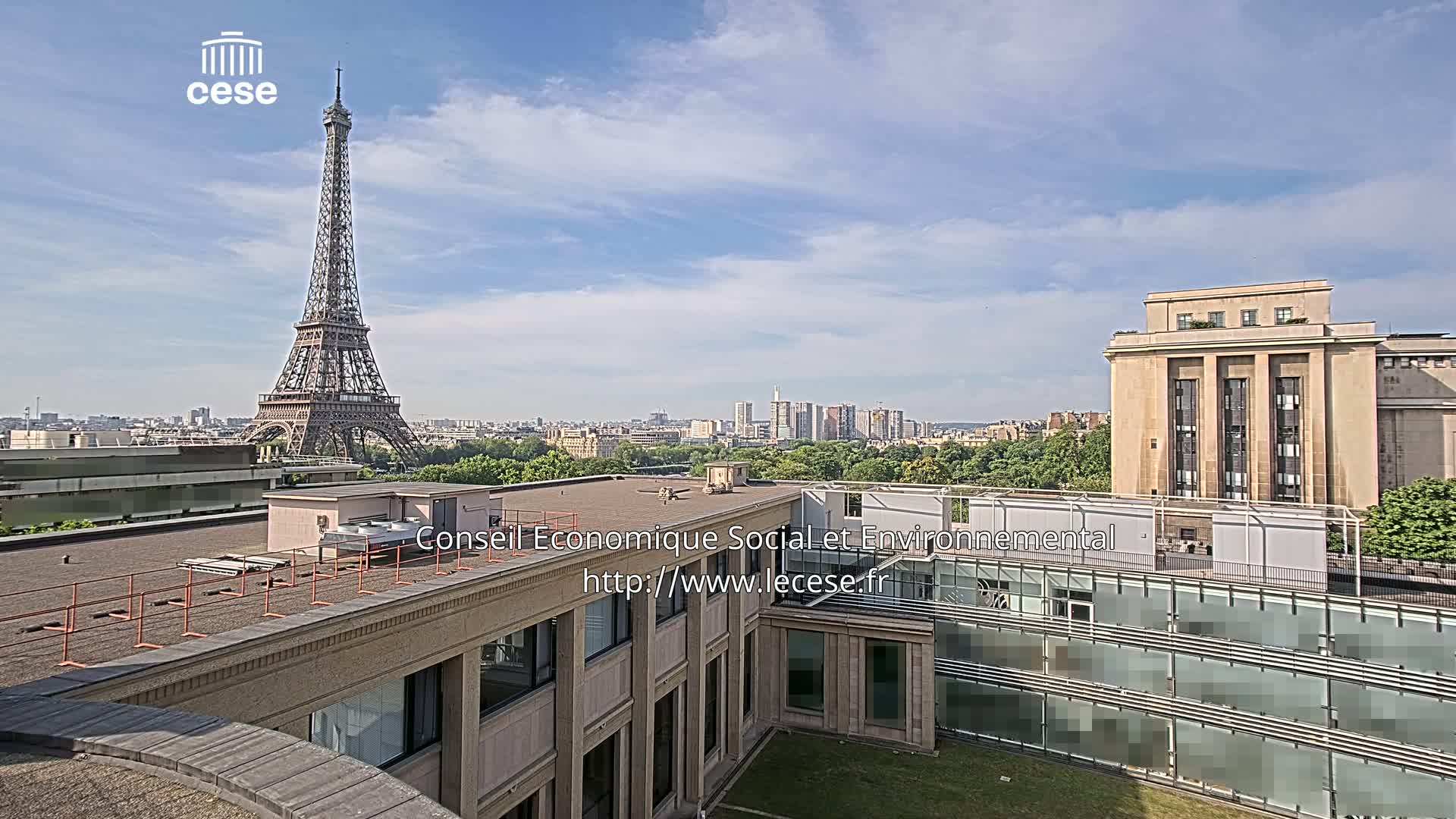 A rooftop view of Parisian buildings and the Eiffel Tower on a partly cloudy day.