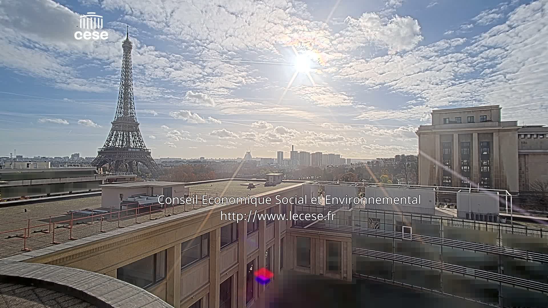 An outdoor view of the Eiffel Tower in the distance under a cloudy sky, with a modern building and cityscape in the foreground.