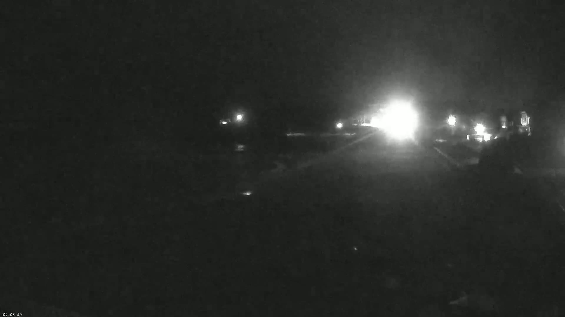 A nighttime, low-light view of a roadway with several vehicles' headlights visible in the distance.