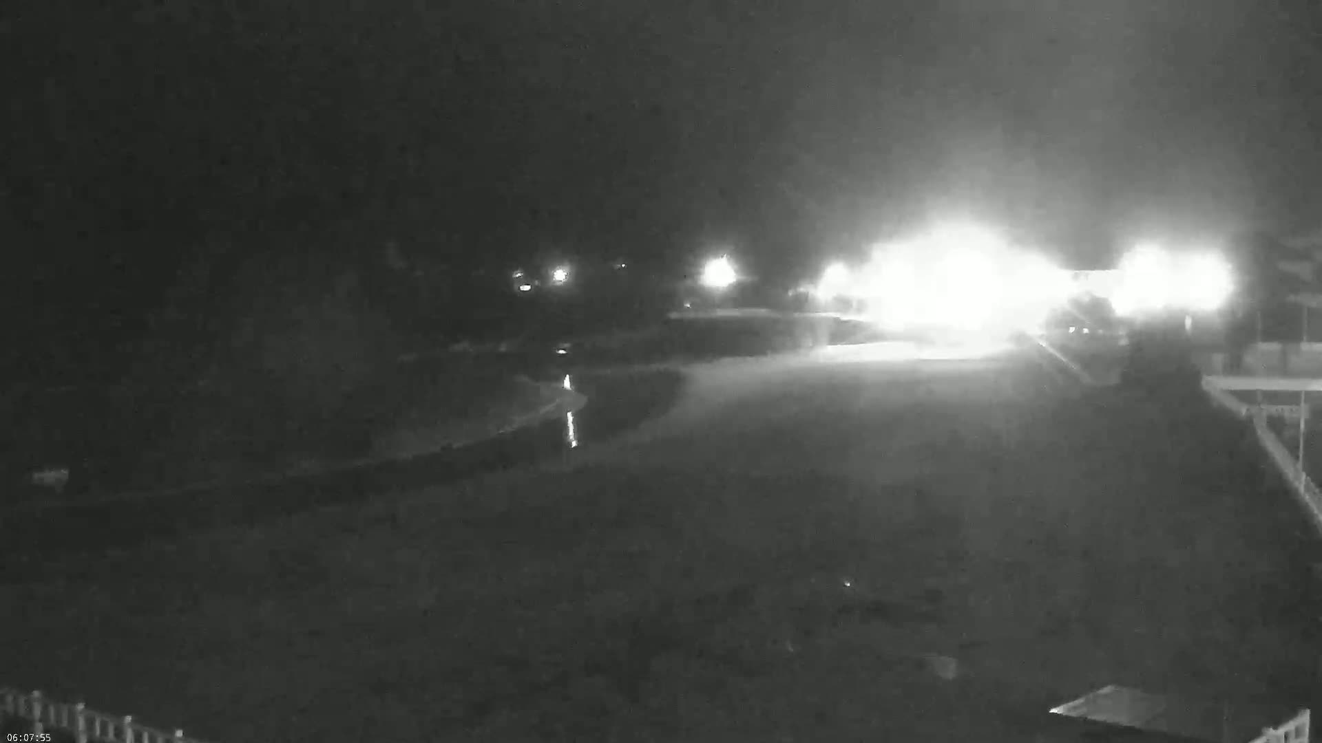 A nighttime, low-light view shows a dimly lit roadway with bright headlights approaching from the distance.