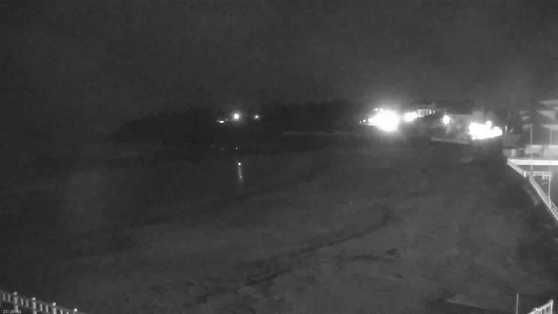 A nighttime, low-light view of a dark body of water next to a shoreline with some buildings visible in the distance.