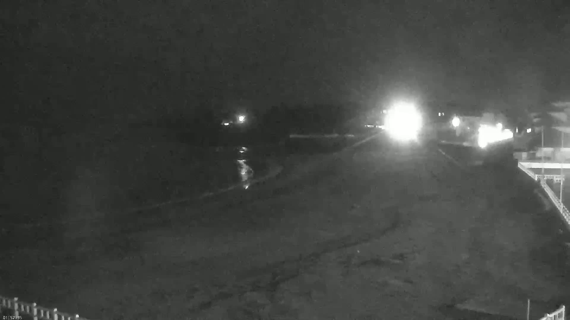 A nighttime, low-light image shows a dark beach with a road and distant headlights visible.