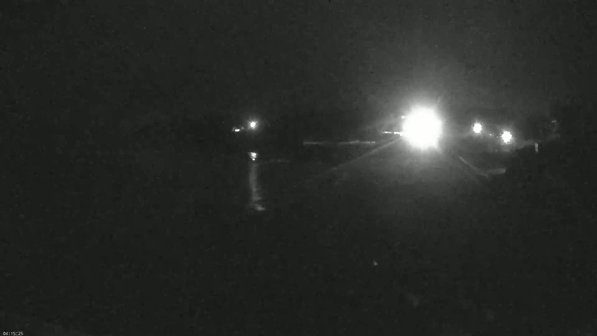 At night, vehicle headlights illuminate a dark road and surrounding area.