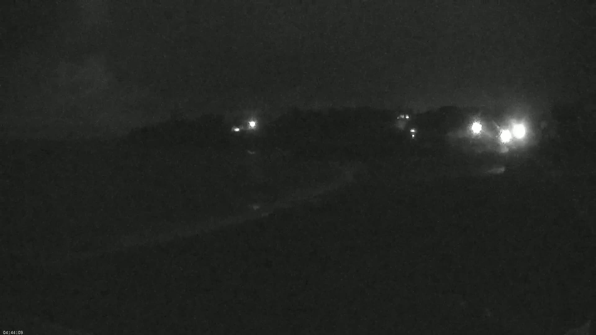 A nighttime, low-light view of a dark landscape with a few distant lights visible.
