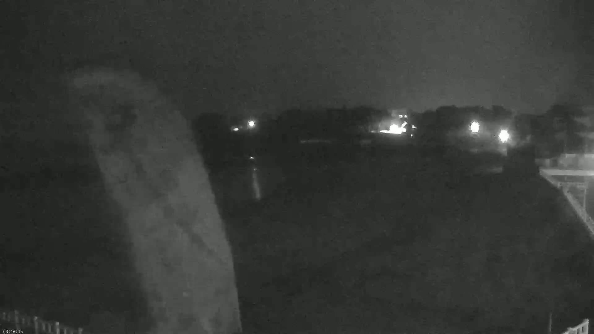 A nighttime, low-light image shows a blurry, dark foreground with a few distant lights visible across a dark landscape.