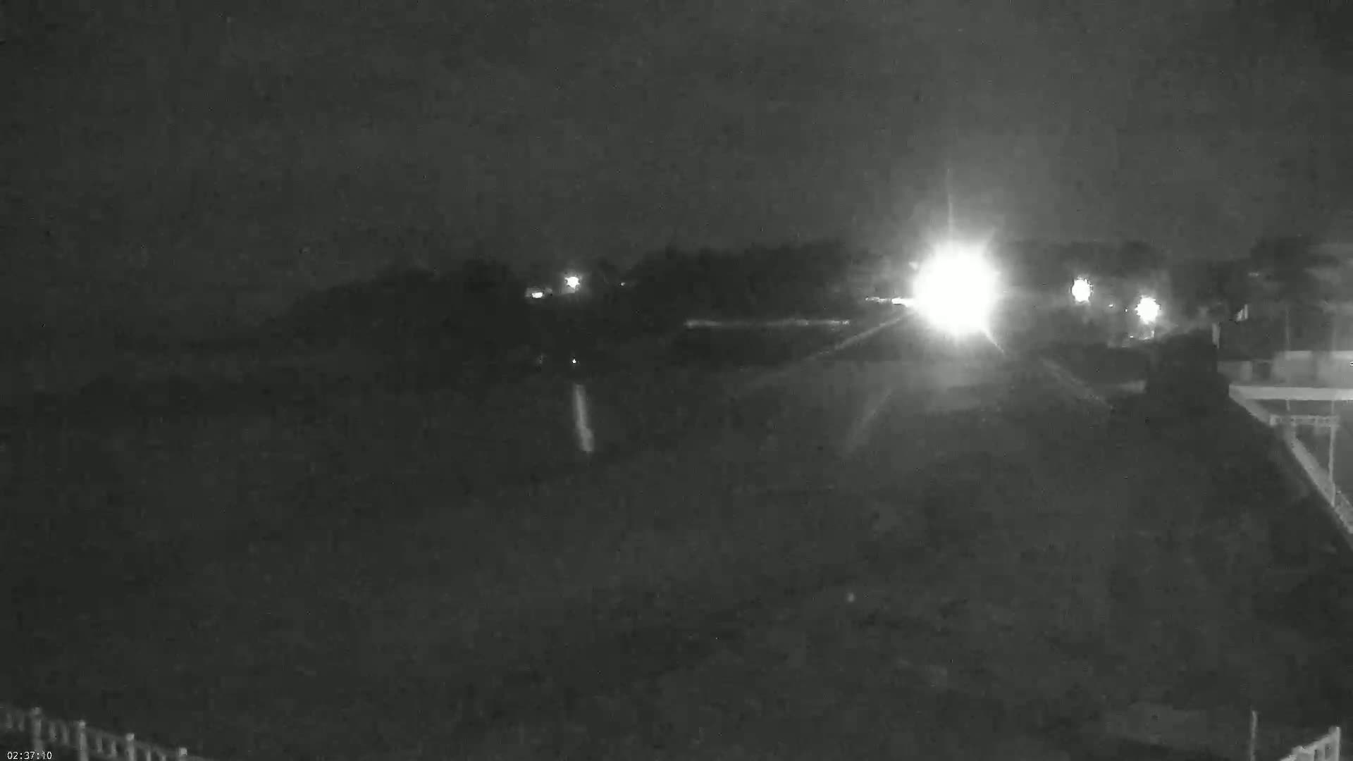 A nighttime, low-light view shows a dark landscape with a few distant lights from vehicles and buildings.