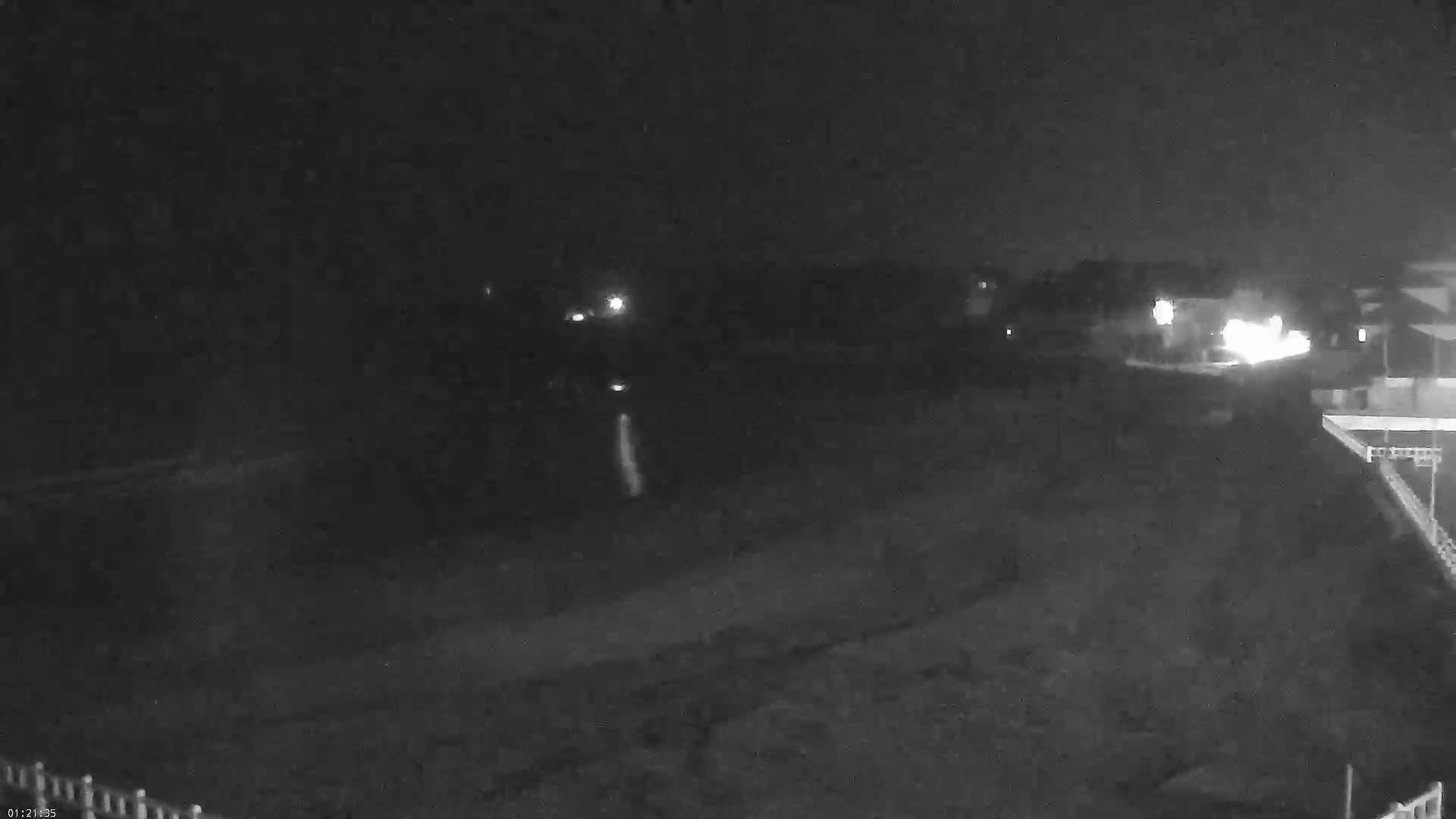 A nighttime, low-light view shows a dark, empty area with a few distant lights and a portion of a building visible in the lower right.