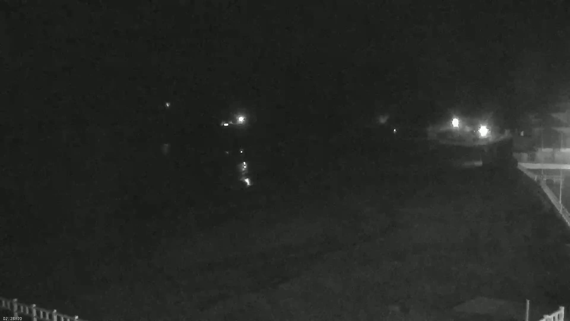 A nighttime, low-light view of a dark body of water with a few distant lights visible along the shoreline.