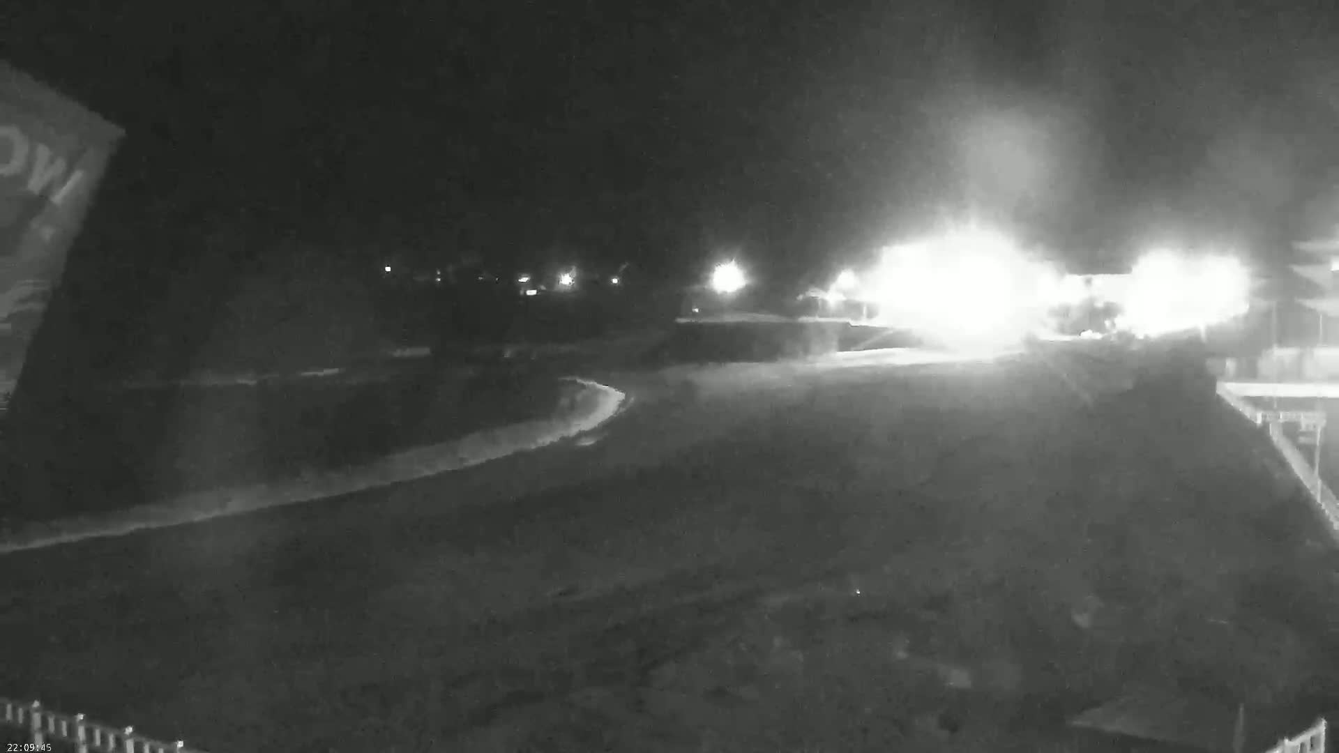A nighttime, low-light view of a curved road with bright lights in the distance and some hazy or foggy conditions.