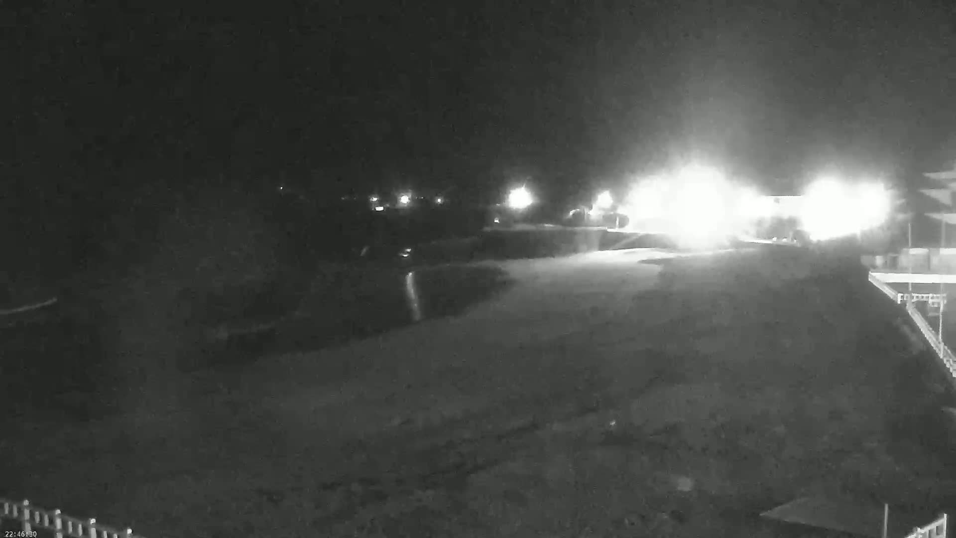 A nighttime, low-light view of a mostly empty roadway with bright lights in the distance.