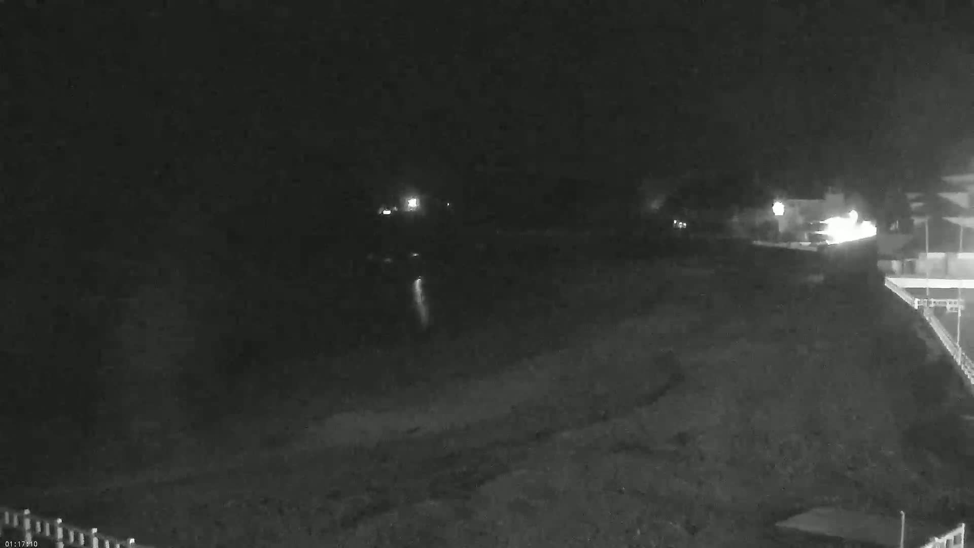 A dark, nighttime scene shows a dimly lit shoreline with a few lights visible in the distance.