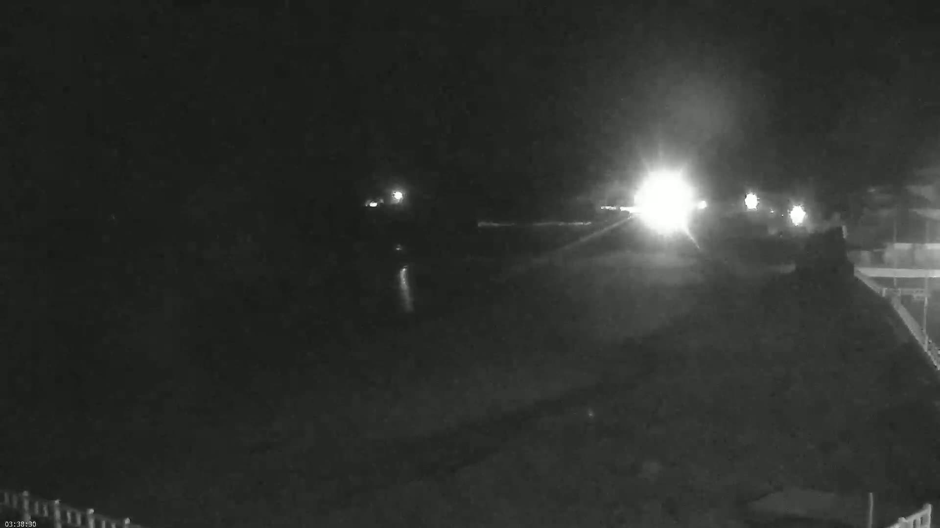 A nighttime, low-light view shows a road with vehicle headlights in the distance.