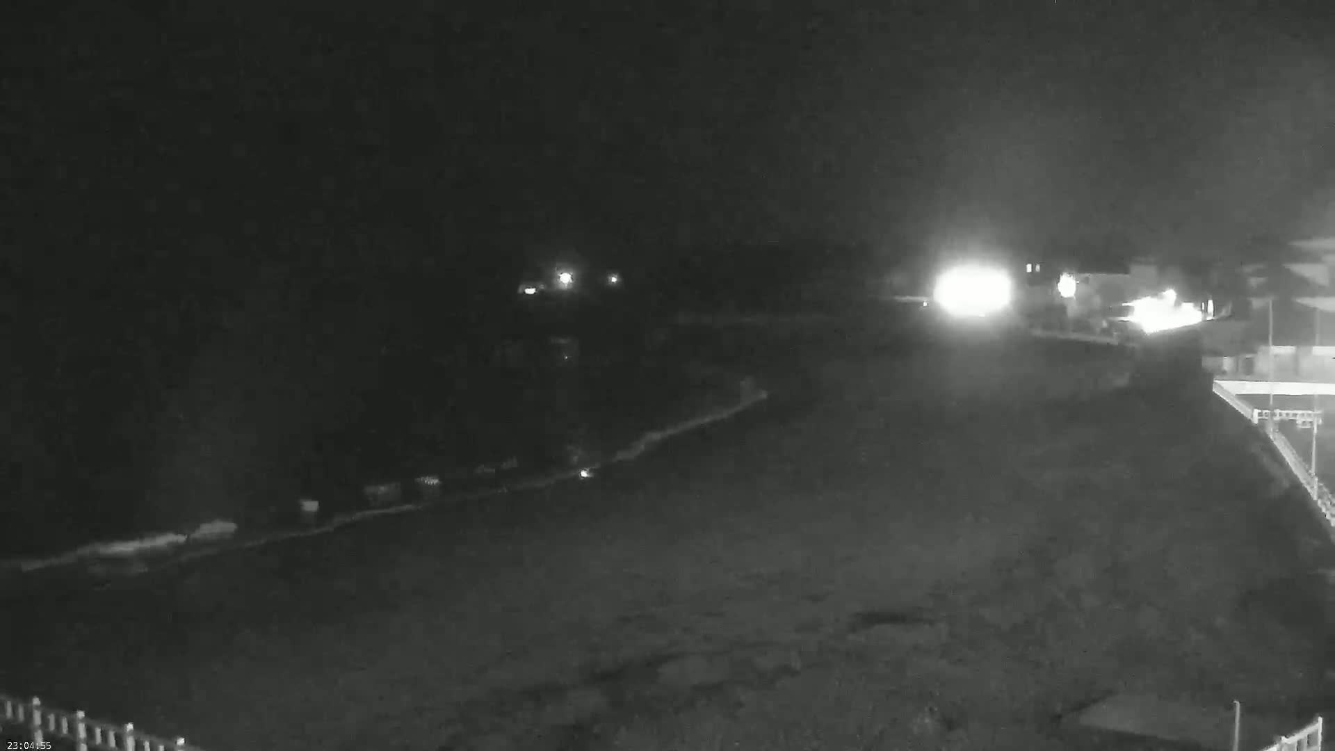 A nighttime, low-light view of a dark beach with some distant lights and a building visible to the right.