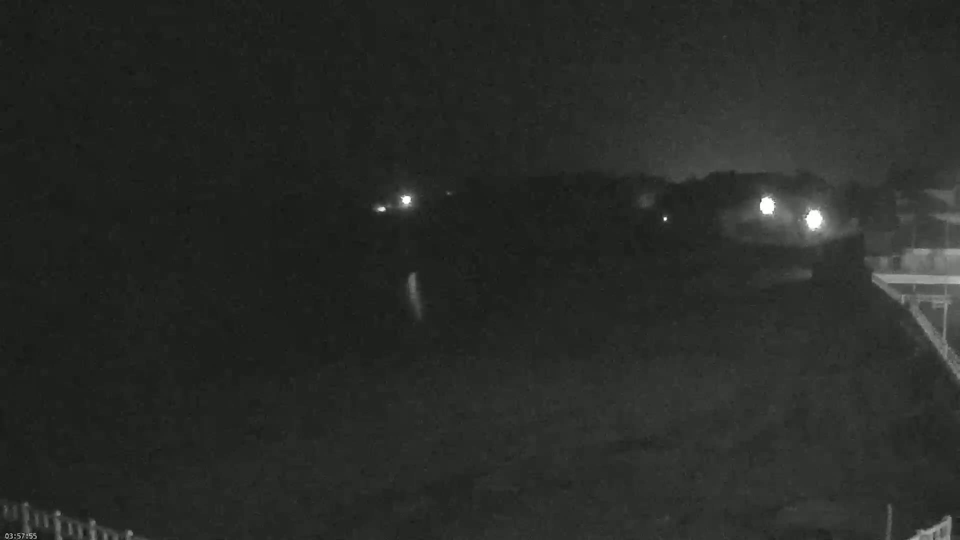 A nighttime, low-light view shows a dark expanse of land with a few distant lights, possibly from houses or streetlights.