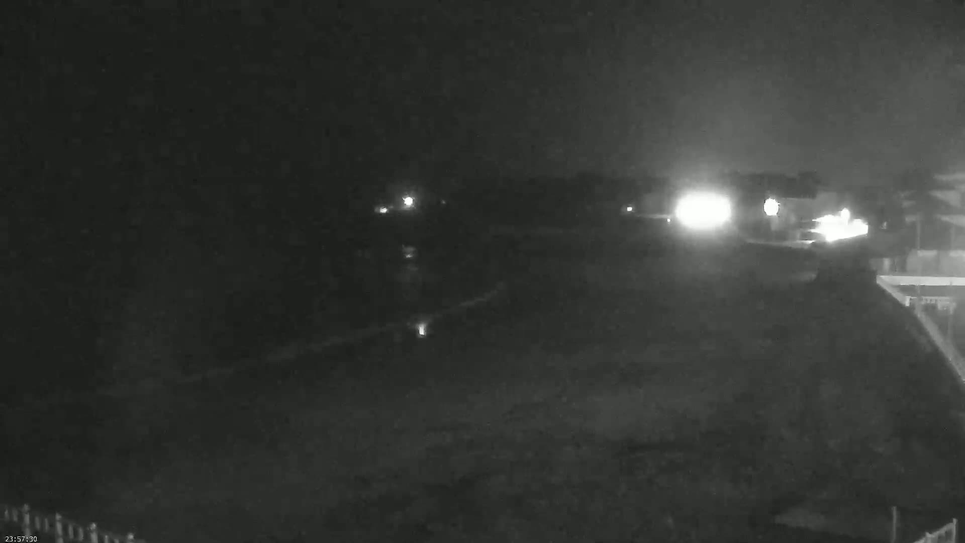 A nighttime, low-light view shows a dark, flat expanse of land with a few distant lights visible.