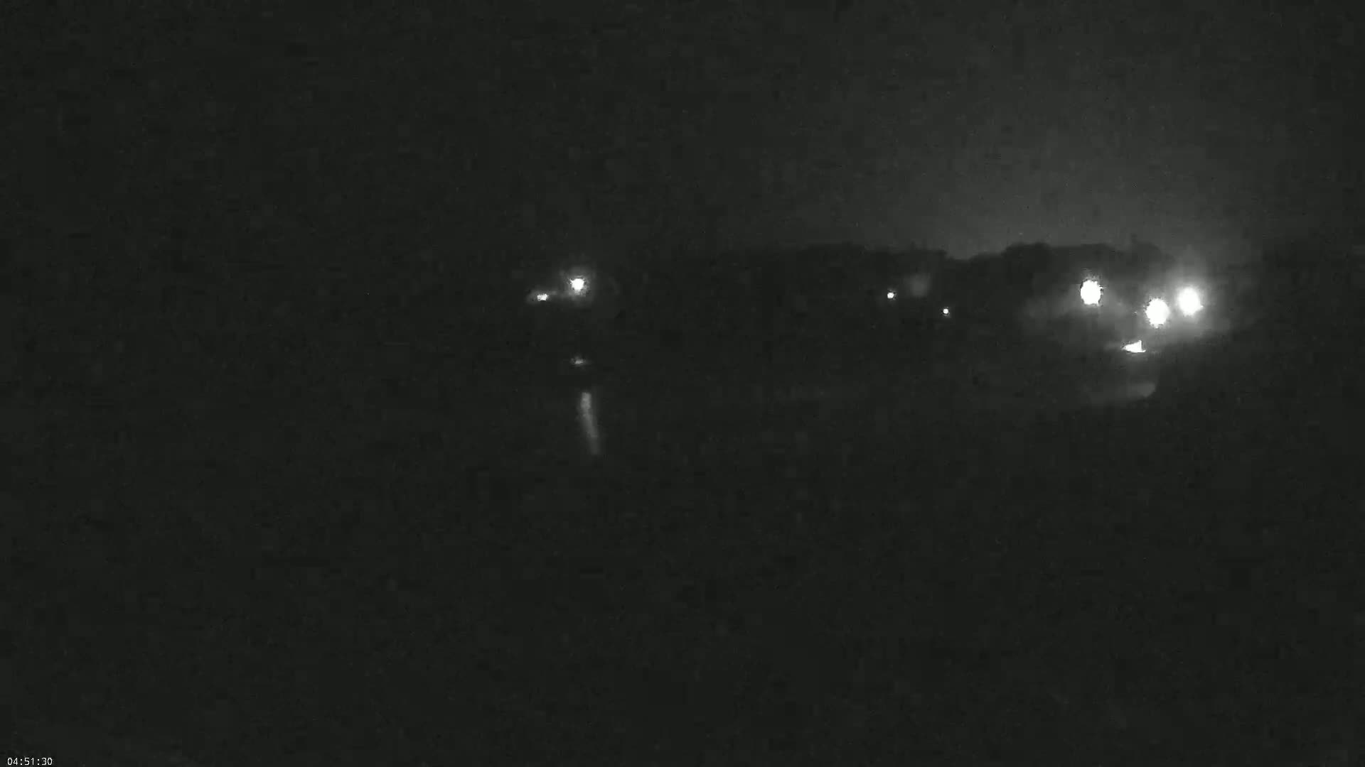 At night, several sets of vehicle headlights are visible in the distance, illuminating a dark, possibly wooded area.