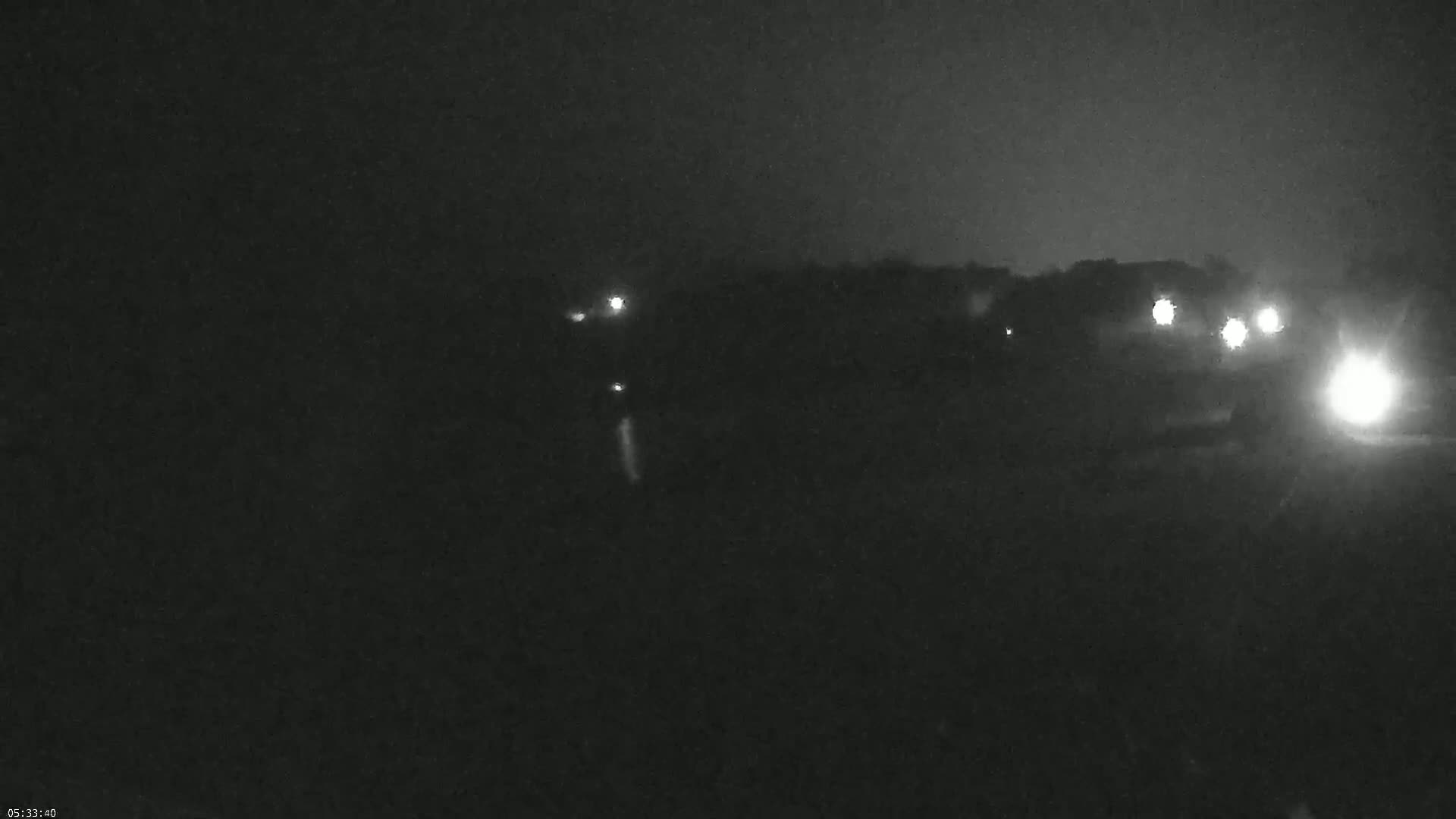 At night, several sets of vehicle headlights are visible in the distance, traveling along a dark road.