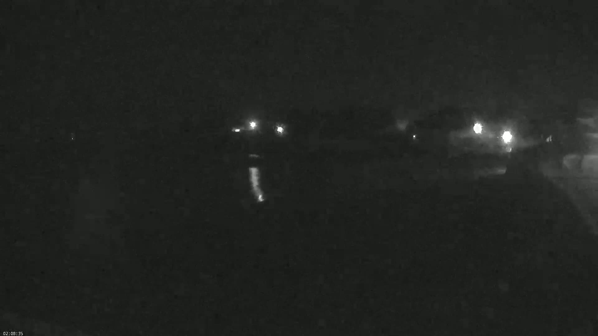 A dark nighttime scene shows a few distant lights, possibly from vehicles or buildings, under a cloudy sky.