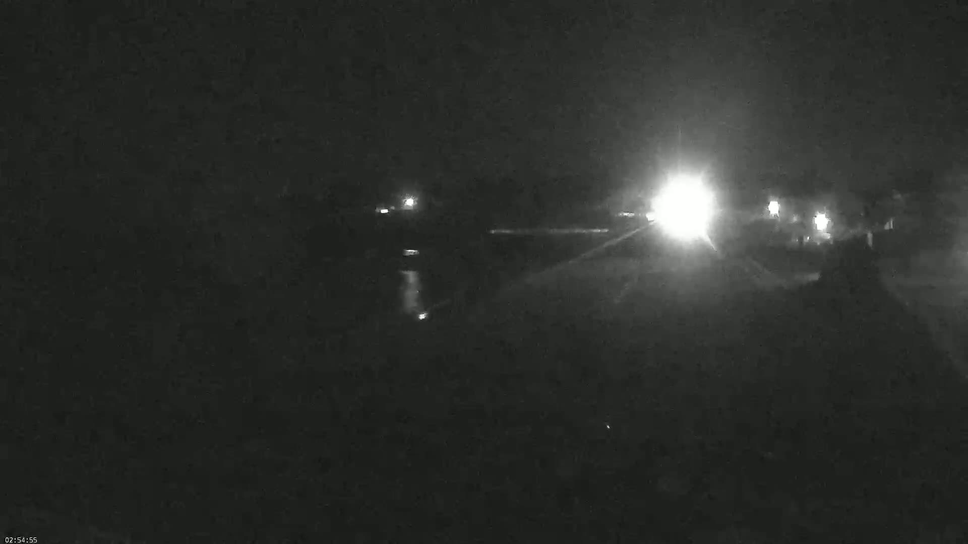 A nighttime, low-light view shows a dark roadway with bright headlights approaching from the distance.