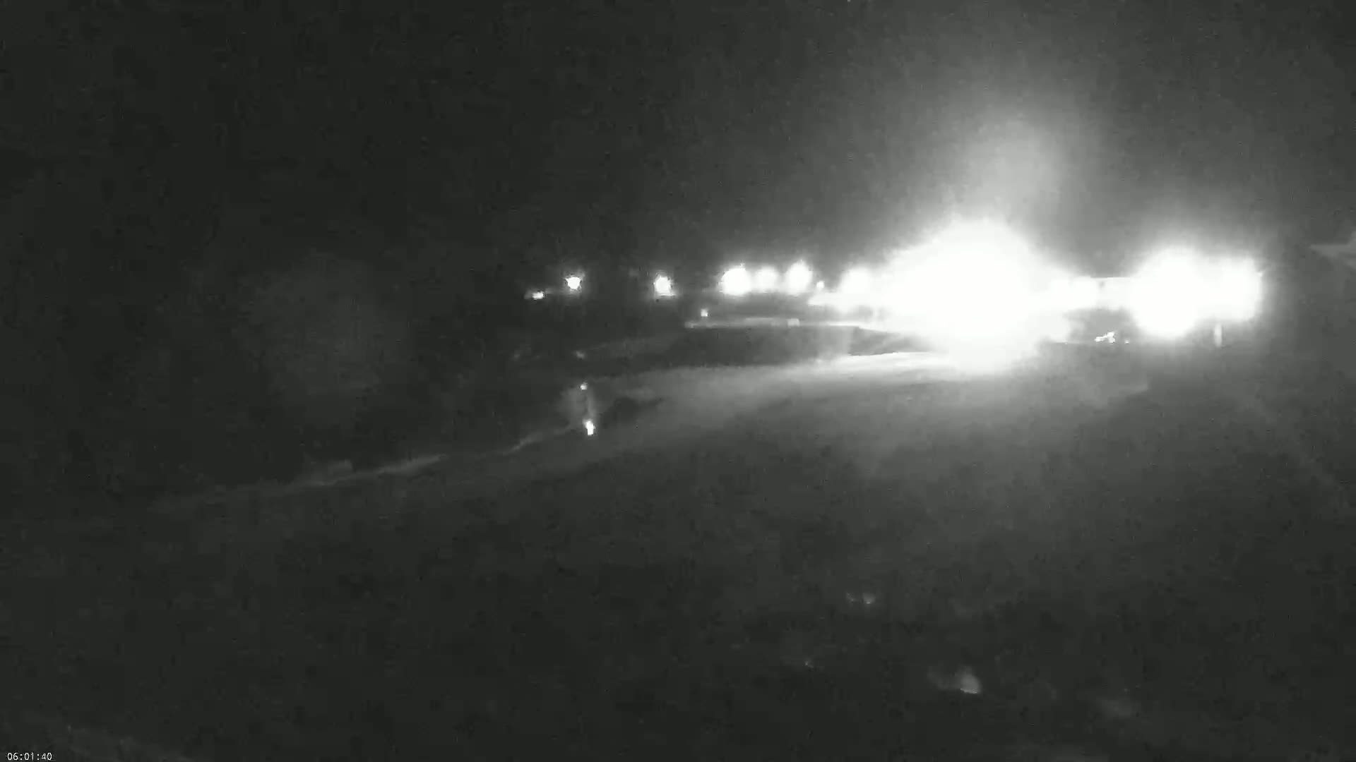 A nighttime, low-visibility scene shows bright headlights of vehicles approaching from a distance on a road.