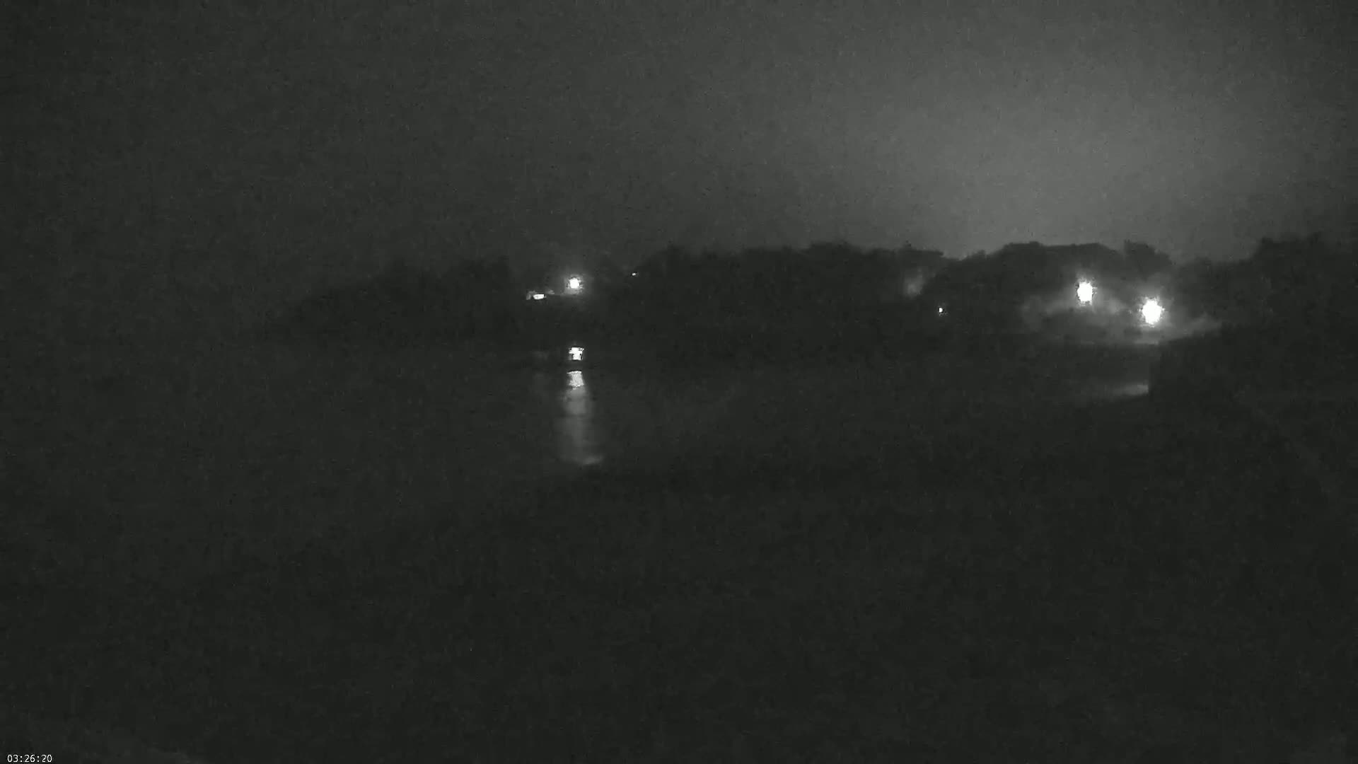 A nighttime, dark, and blurry view of a shoreline with faint lights visible in the distance.