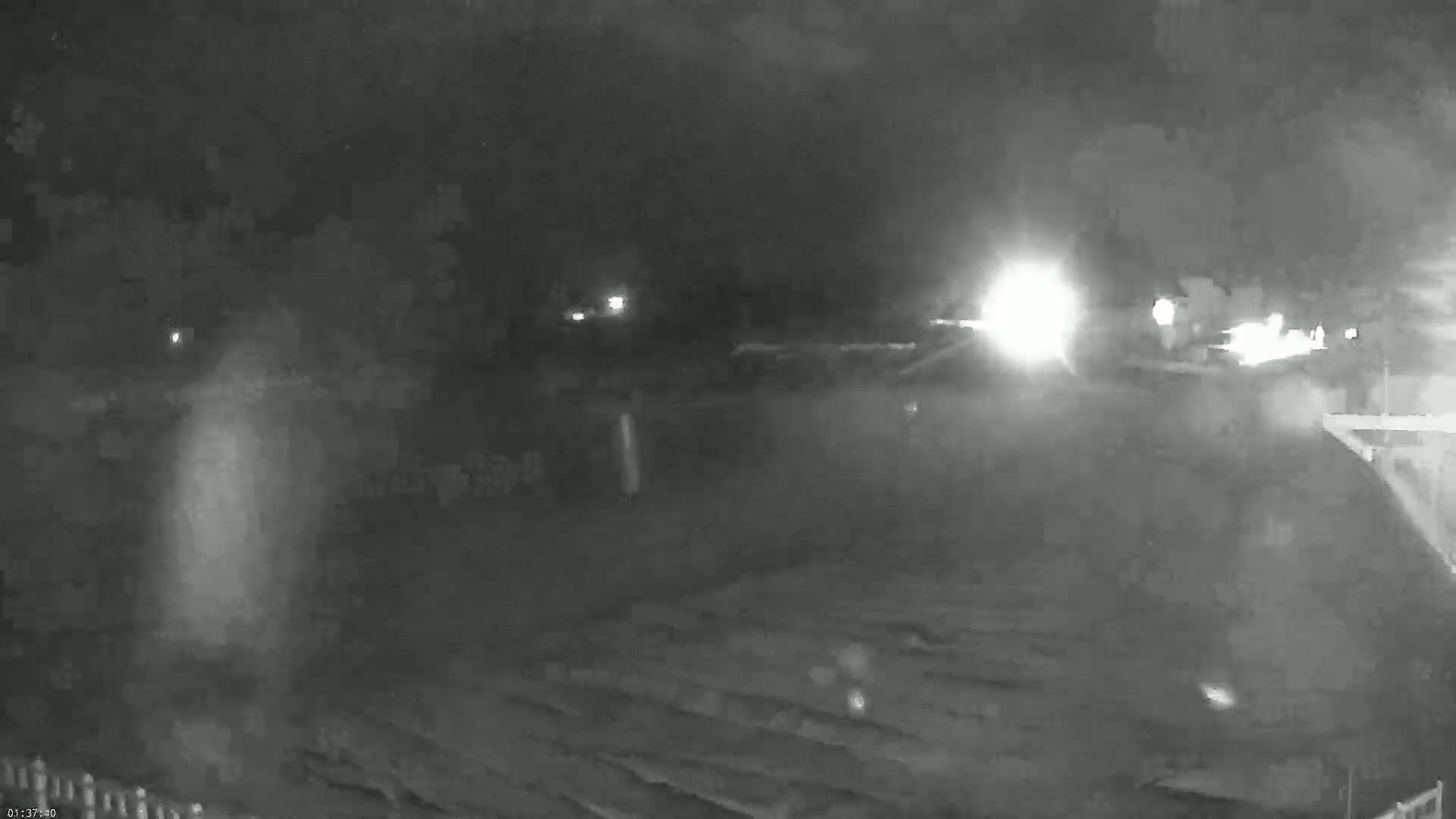A nighttime, low-light view of a mostly empty parking lot with some distant headlights visible.