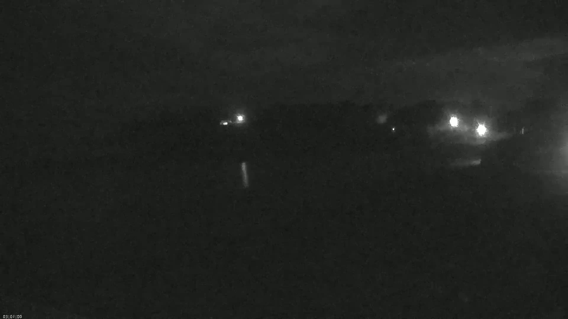 A dark, nighttime scene shows a few distant lights in the middle distance, possibly from vehicles or buildings.