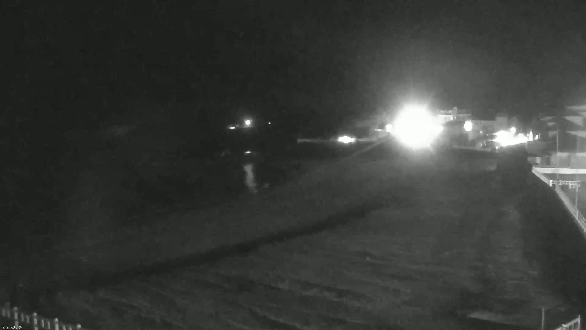 A nighttime, low-light view shows a dark expanse of land with a few distant lights and a brighter area possibly indicating a road or building in the background.