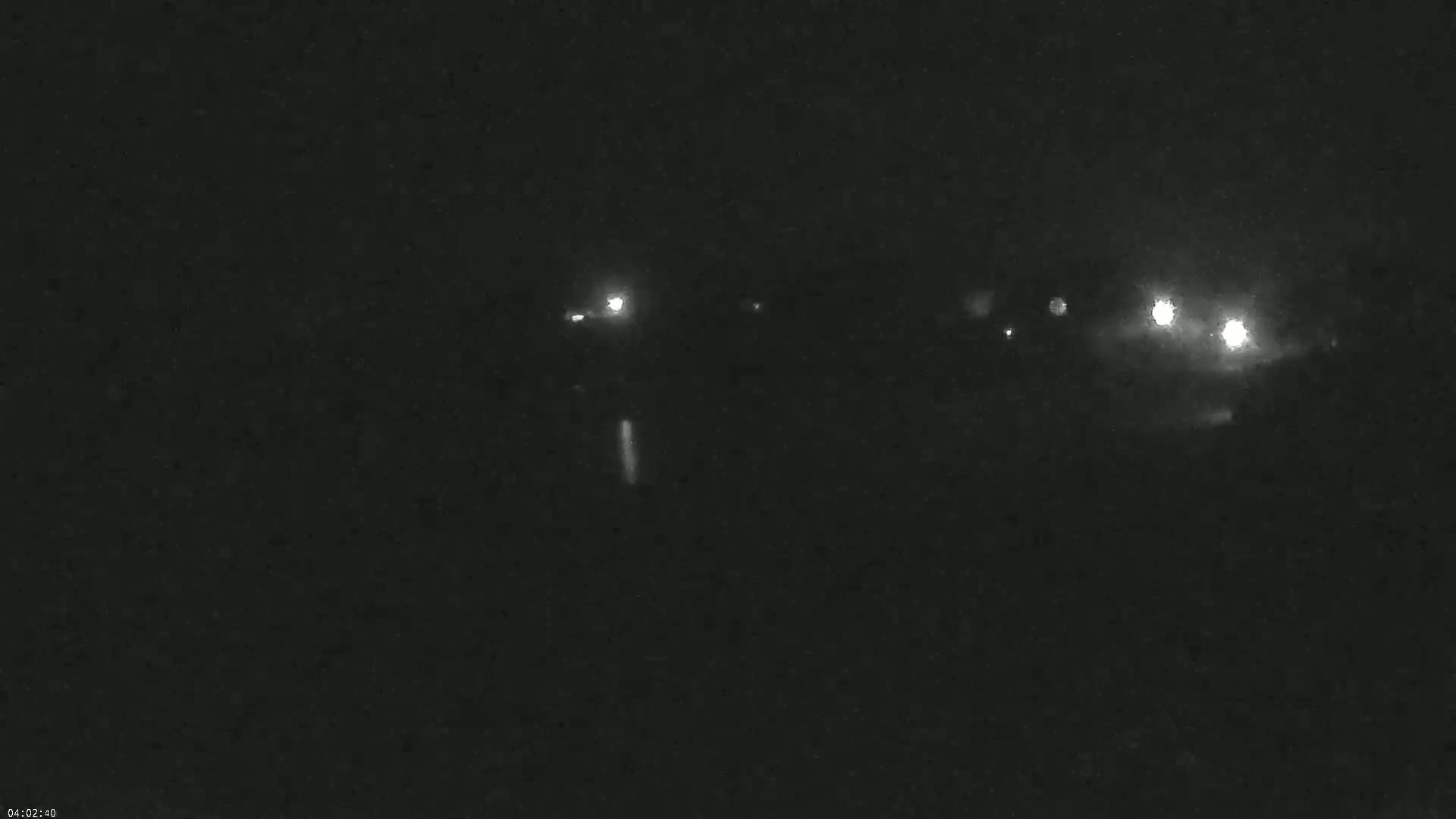 A nighttime, low-light image shows several faint lights in the distance, possibly from vehicles, under dark conditions.