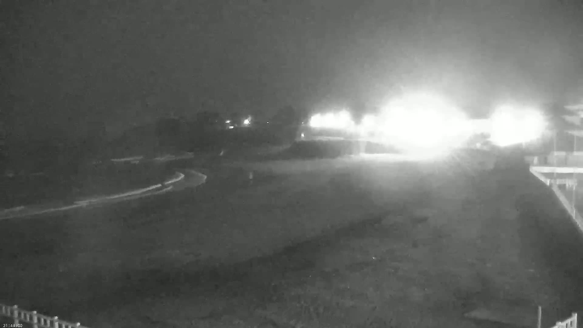 A nighttime, hazy view of a roadway curving through a dimly lit area with bright lights in the distance.