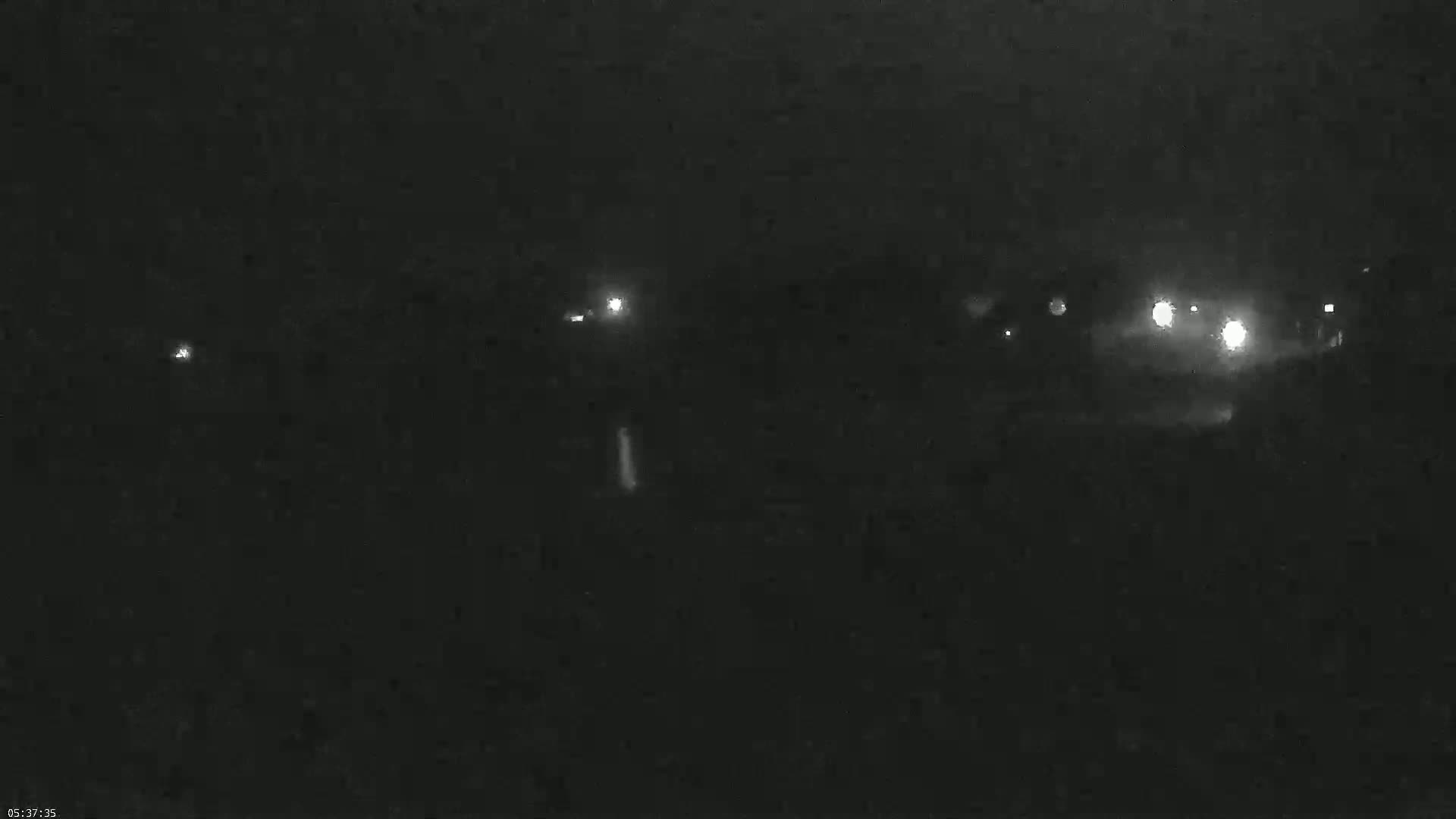 A nighttime, low-light view shows several distant headlights from vehicles and faint lights in the darkness.