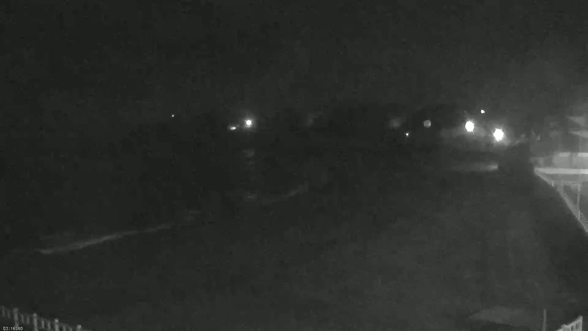 A nighttime, low-light image shows a dark, mostly empty area with a few distant lights visible in the background.