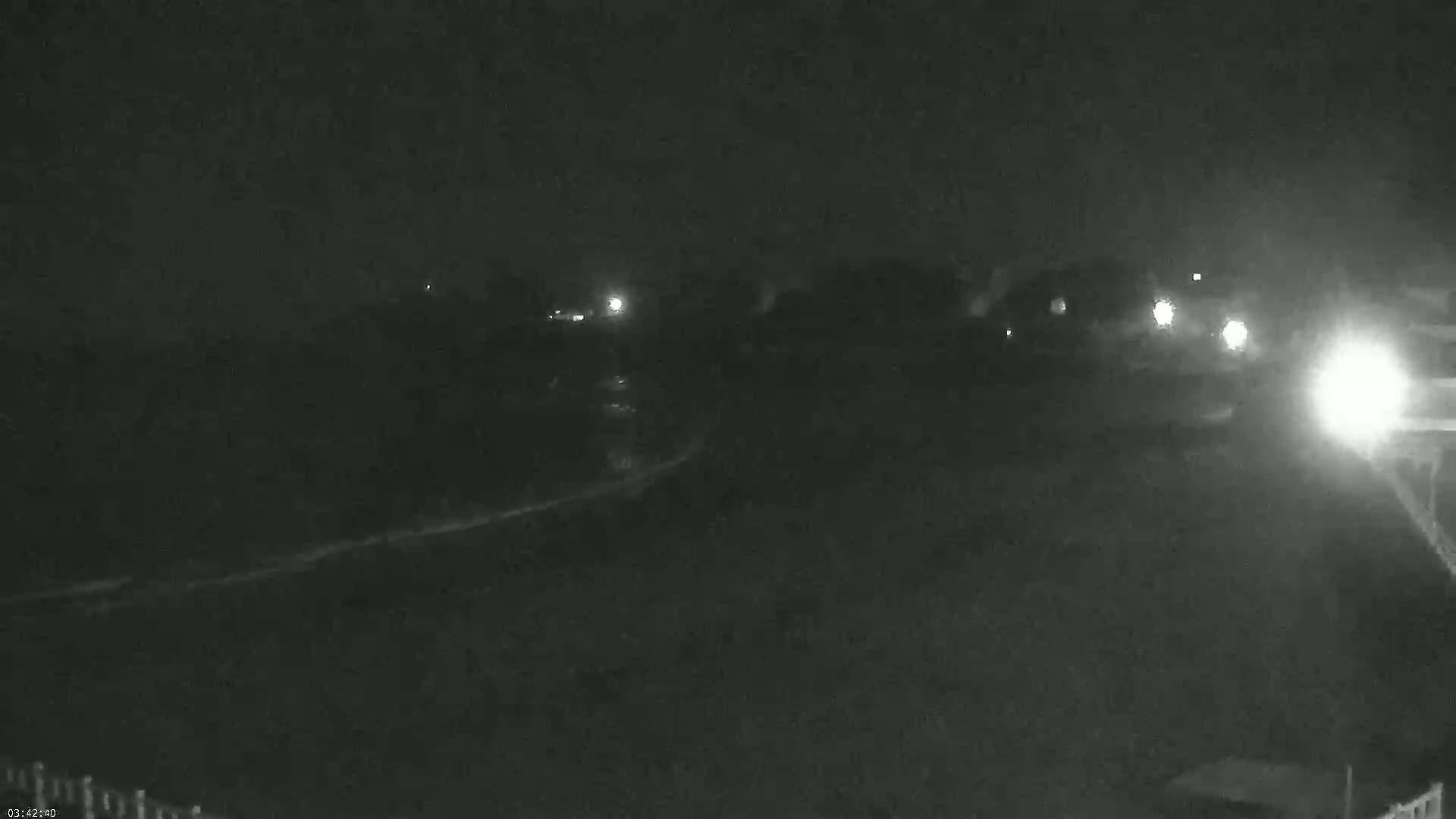A nighttime, low-light view shows a dark landscape with a few distant lights and what appears to be a body of water in the foreground.