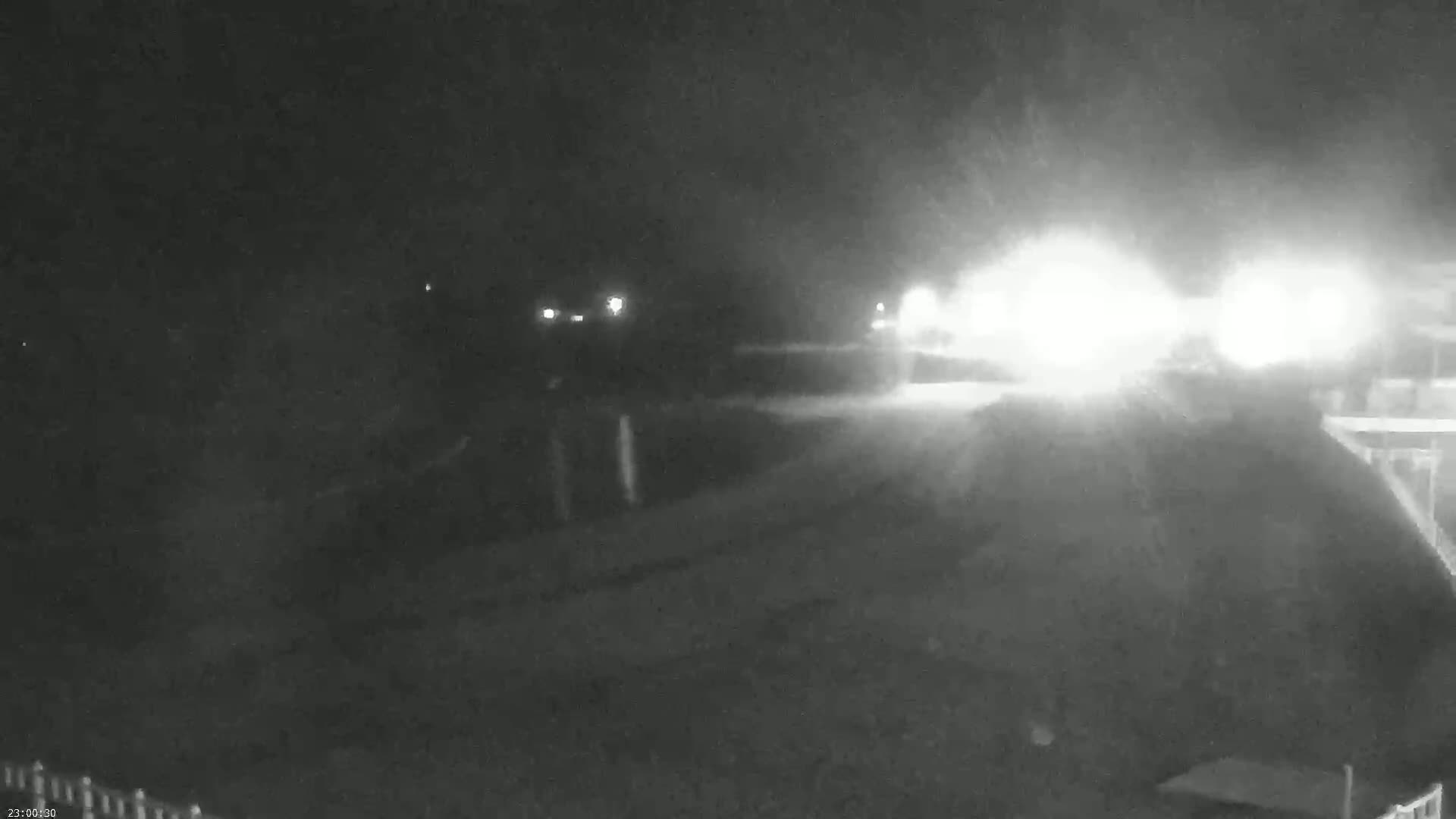A nighttime, low-light view shows a road with headlights approaching from the distance.