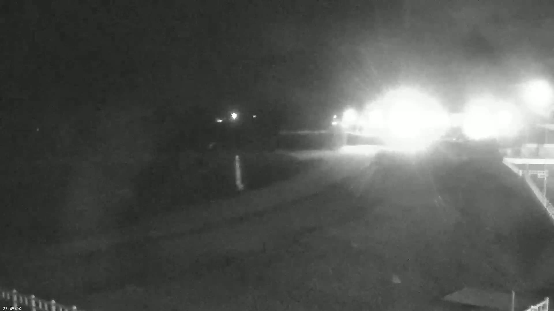 A nighttime, blurry view shows a roadway with bright headlights approaching from the distance in foggy or snowy conditions.