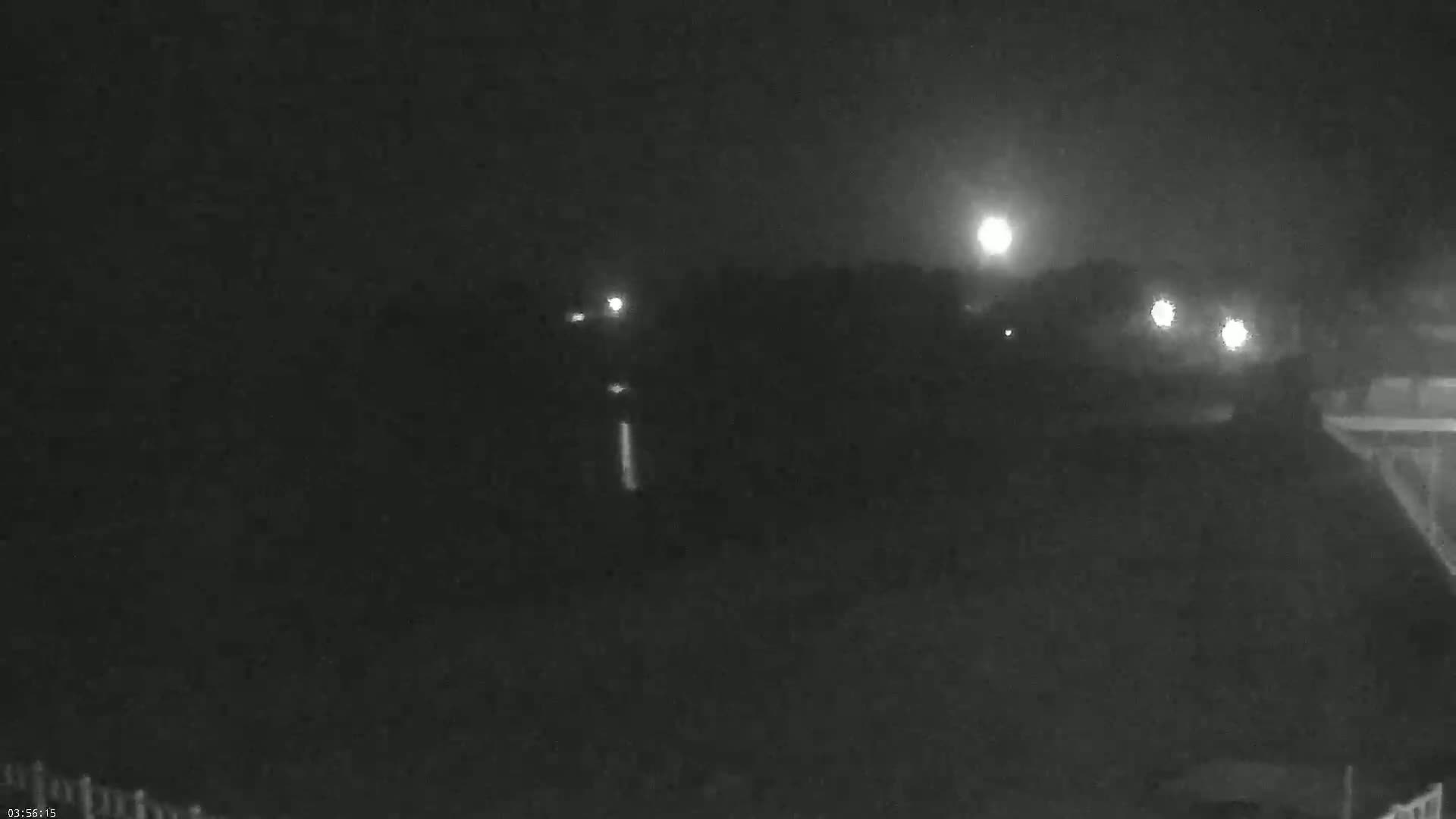 A nighttime, hazy view shows a dimly lit road with distant lights and dark vegetation.