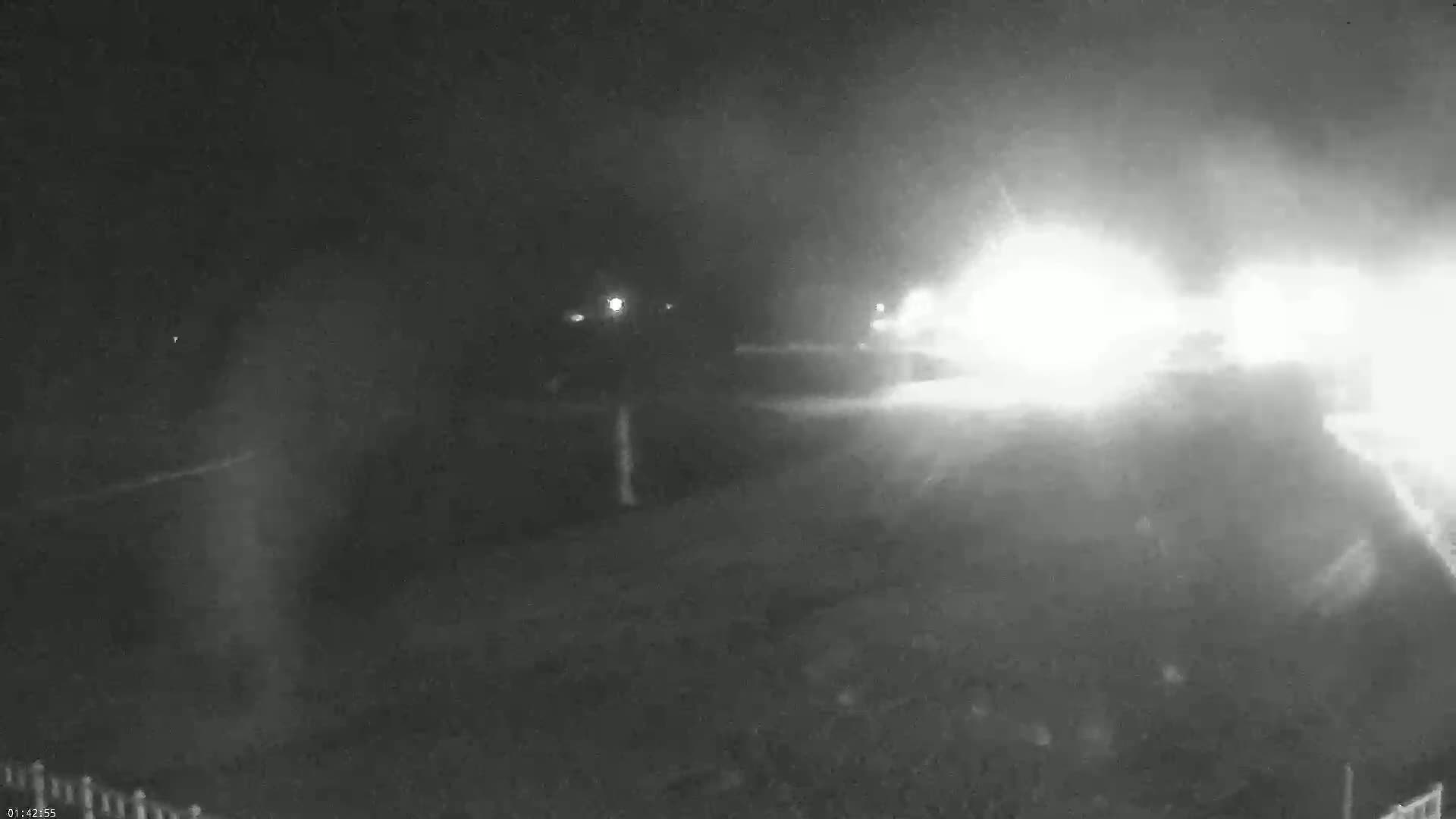 A nighttime, blurry, low-light image shows a hazy or foggy scene with bright lights in the distance.