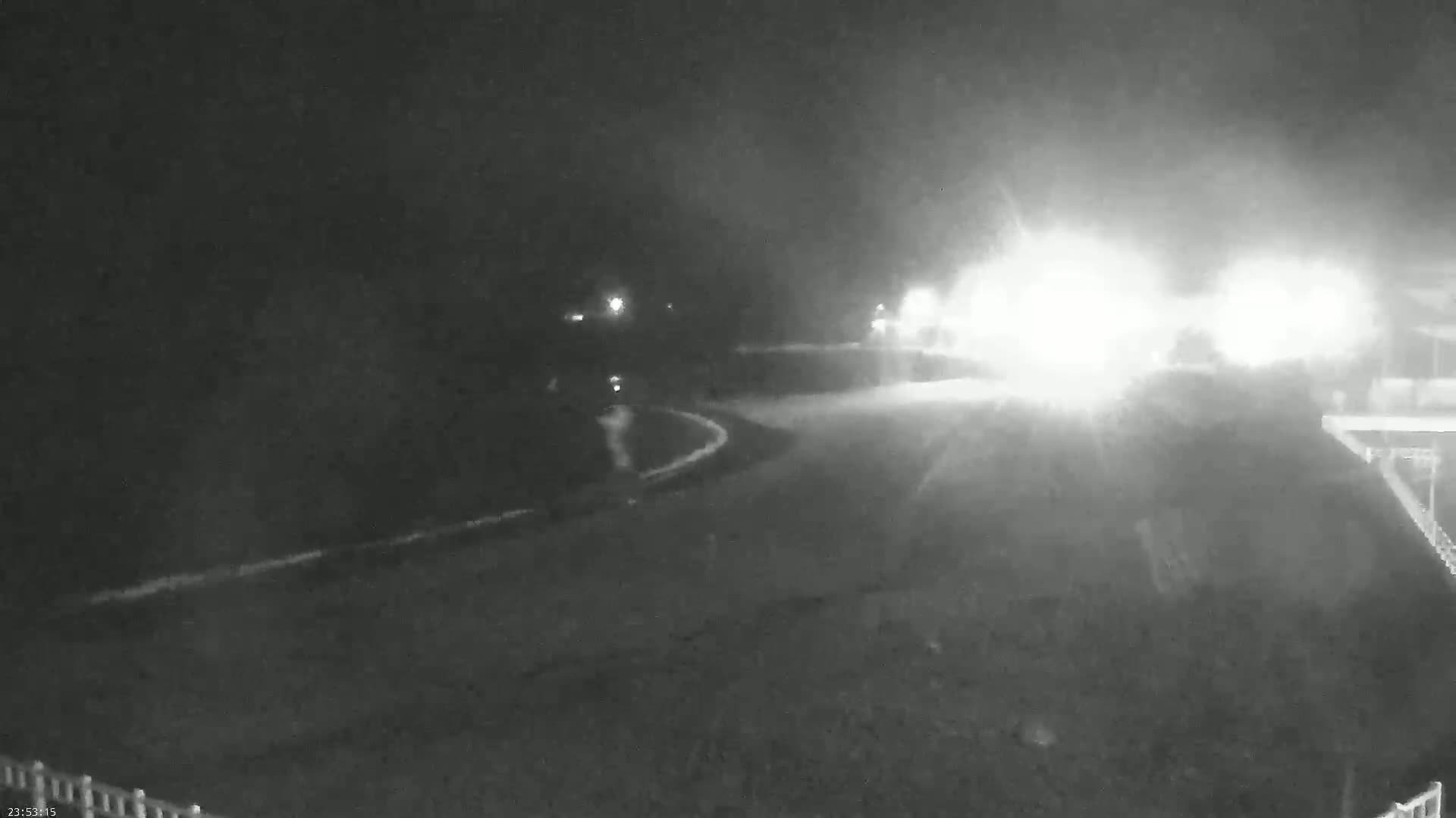 A nighttime, low-visibility scene shows a roadway curving to the left with bright headlights approaching from the right.