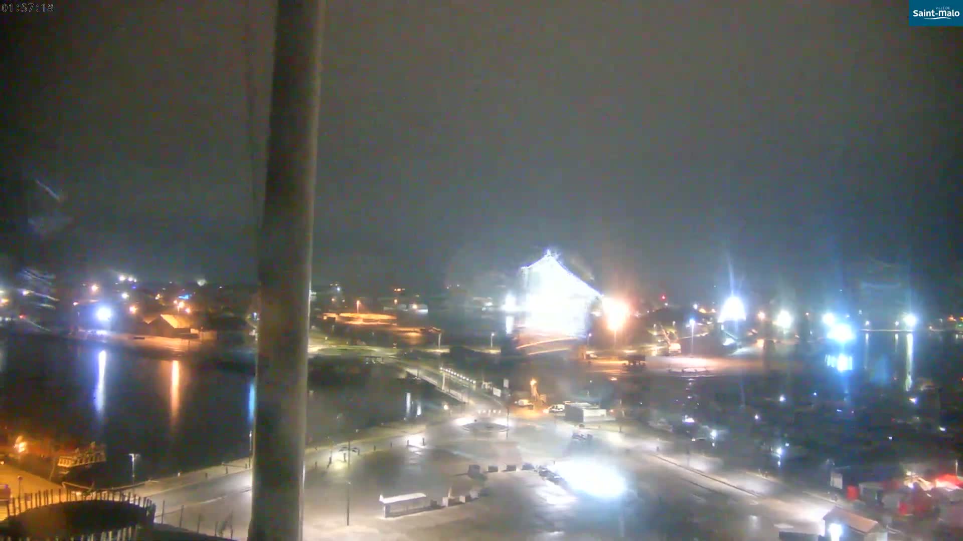 A nighttime view of a harbor and city, illuminated by lights, under hazy or foggy conditions.